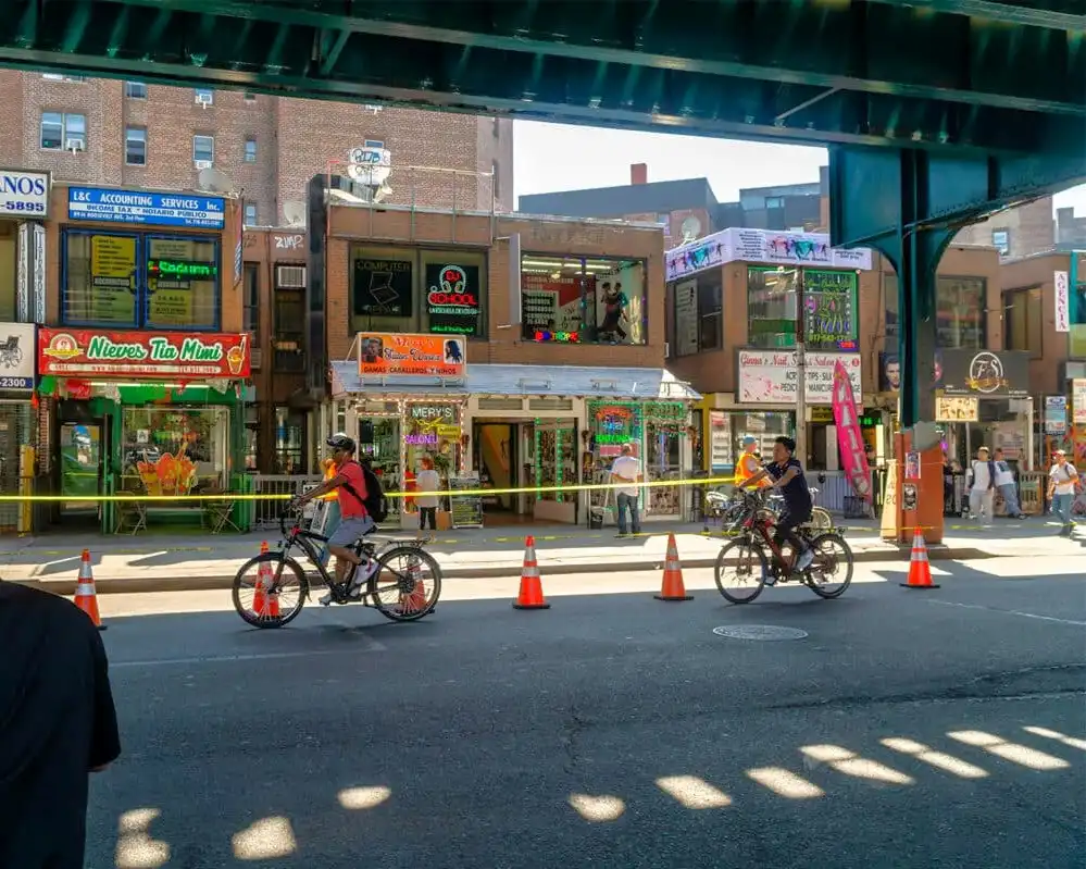 10_nycsecreto_trenelevado Imagen de Roosevelt Ave en Queens Nueva York con la estructura del metro elevado por encima de la calle y dos personas andando en bicicleta