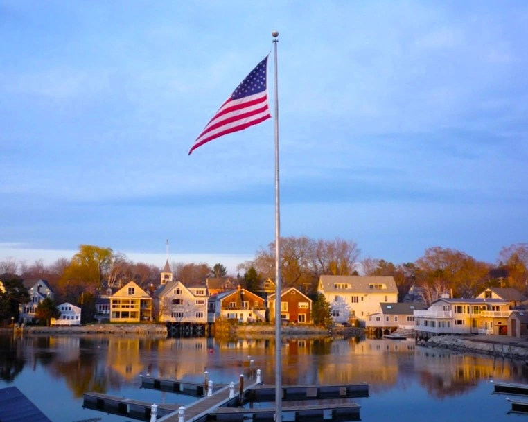 12_lunademiel_kennebunkport Paisaje de Kennebunkport en Maine con las típicas casa de Nueva Inglaterra reflejándose en el agua con la bandera de Estados Unidos en el centro.