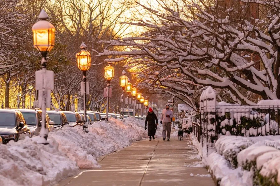 Dos personas caminando por Beacon Hill con las calles nevadas y las farolas encendidas