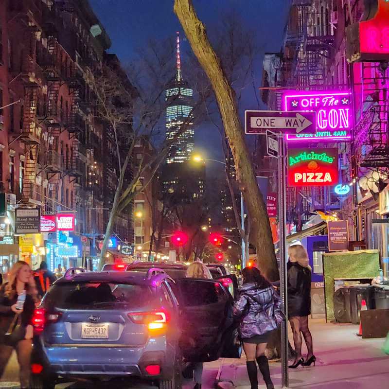 6_manhatan_gratis Mac Dougal Street en Manhattan de noche con carteles de neón y el World Trade Center detrás