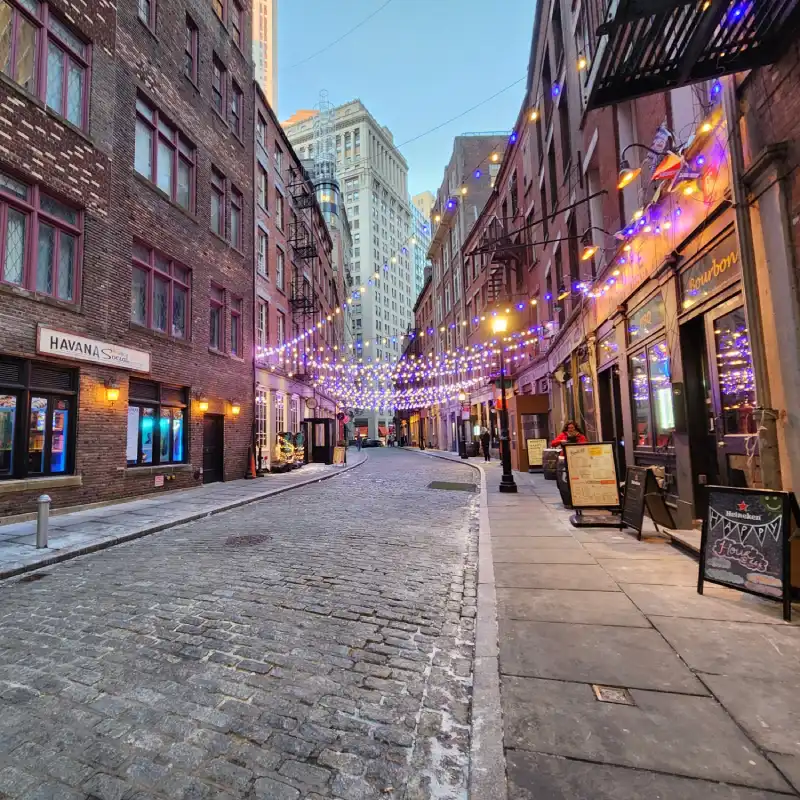 7_manhatan_gratis Stone Street, Manhattan. Calle empedrada con edificios antiguos de ladrillos rojos y una guirnalda de luces cruzando la calle.