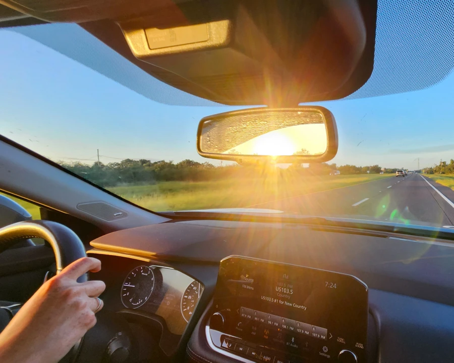 El sol del amanecer reflejando en el espejo retrovisor de un auto con la ruta delante